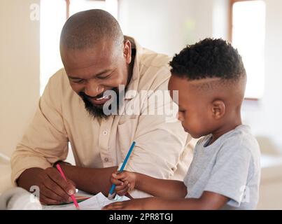 Ein afroamerikanischer Junge macht Hausaufgaben mit seinem Vater. Ein gutaussehender Schwarzer, der seinem Sohn bei der Schularbeit zu Hause hilft. Es ist wichtig, zu lernen und eine Ausbildung zu erhalten. Ein über- und untergeordnetes Element, das an einem Projekt arbeitet Stockfoto