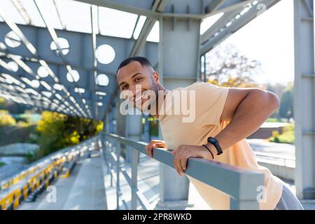 Nahaufnahme. Porträt eines jungen afroamerikanischen Sportlers, der im Stadion stand, Liegestütze an der Bar machte, seine Arme schwingte, die Kamera lächelte. Stockfoto