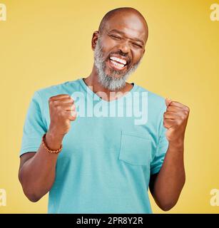 Ein erwachsener afrikanischer Mann, der beim Feiern begeistert aussah, indem er eine Faustbewegung mit den Händen machte und vor einem gelben Studiohintergrund jubelte. Erfolg und Feiern verleihen dem Leben Leidenschaft und Sinn Stockfoto