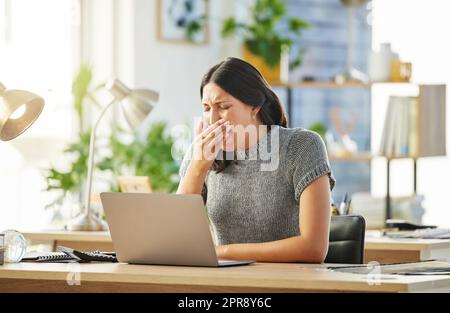 Jemand braucht ein Nickerchen. Eine junge Geschäftsfrau gähnt an ihrem Schreibtisch. Stockfoto