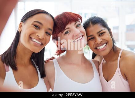 Lass deine Seele leuchten. Porträt einer Gruppe sportlicher junger Frauen, die in einem Yoga-Studio gemeinsam Selfies machen. Stockfoto