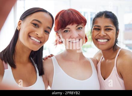 Die glühenden Mädchen. Porträt einer Gruppe sportlicher junger Frauen, die in einem Yoga-Studio gemeinsam Selfies machen. Stockfoto