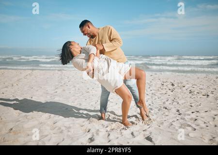 Liebevolles junges gemischtes Paar, das am Strand tanzt. Glücklicher junger Mann und verliebte Frau genießen romantische Momente während der Flitterwochen am Meer Stockfoto