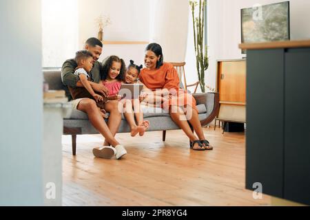 Eine glückliche gemischte Familie von fünf Personen, die sich zu Hause auf dem Sofa entspannen. Die schwarze Familie liebt es, auf dem Sofa liebevoll zu sein, während sie ein digitales Tablet verwendet und streamt. Ein junges Paar, das sich mit seinen Kindern anfreundet und zu Hause Filme ansieht Stockfoto