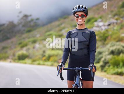 Eine sportliche junge Frau, die draußen radelt. Sportliche Passform für Frauen, die Helm und Brille tragen, während sie mit dem Fahrrad auf dem Berg trainieren. Lächelnd und glücklich, ein Hobby zu genießen Stockfoto