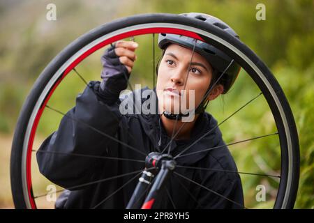 Eine sportliche junge Frau, die das Rad eines Fahrrads repariert, während sie draußen Rad fährt. Sportliche Frau, die einen Helm trägt und den Luftdruck eines Fahrradreifens für Reparaturen prüft, während sie im Freien sportlich unterwegs ist Stockfoto