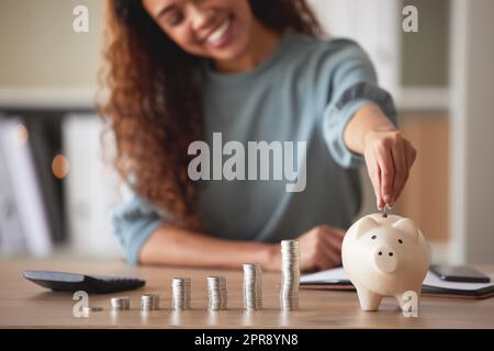 Junge afroamerikanische Frau, die Münzen in eine Schweinebank zu Hause steckt. Gemischte Person, die Münzen zählt, während sie die Finanzplanung in ihrem Wohnzimmer durchführt. Sparen, investieren und an die Zukunft denken Stockfoto