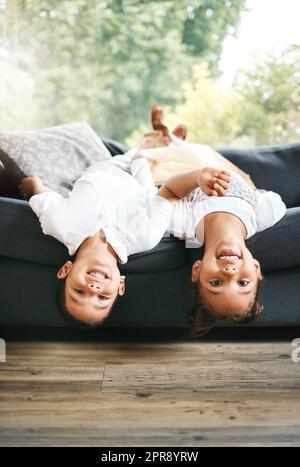 Porträt von zwei kleinen Geschwistern gemischter Rassen, die Zeit miteinander verbringen, kopfüber zu Hause liegen. Süßes hispanisches Mädchen und Junge, die auf der Couch in der Lounge spielen Stockfoto