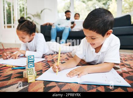 Kleine Jungen und Mädchen malen mit Malstiften auf dem Wohnzimmerboden, während sich ihre Eltern auf dem Sofa entspannen. Kleine Kinder, Schwestern und Geschwister, die sich in der Familienzeit zuhause einfärben Stockfoto