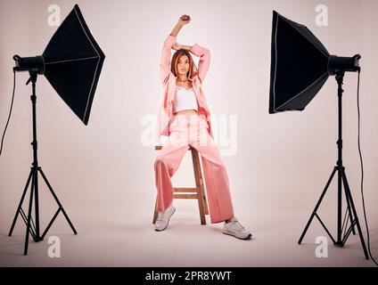 Porträt einer jungen Mischrasse, die sich in trendiger Kleidung posiert, während sie in einem Studioshooting auf einem Stuhl chillt. Hispanische Frau, die die neueste Modesammlung mit coolem Stil und einer coolen Pose zeigt Stockfoto