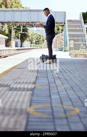 Schwarzer Geschäftsmann, der allein reist. Ein junger afroamerikanischer Geschäftsmann, der auf einen Zug am Bahnhof wartet und sein drahtloses Handy während seines Arbeitsaufenthalts am Bahnhof benutzt Stockfoto