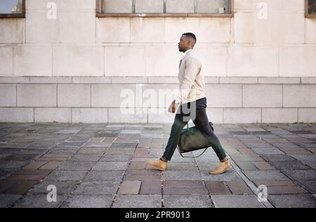 Ein afroamerikanischer Geschäftsmann, der mit seinem Gepäck durch die Stadt läuft und gleichzeitig in der Stadt stilvoll aussieht Stockfoto