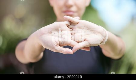 Nahaufnahme einer Sportlerin, die sich an einem sonnigen Tag beim Workout in der Natur die Hände versetzte und gleichzeitig ihre Arme dehnte. Sportliche Sportlerin, die vor ihrem Lauf in der Natur ein Warm-Up-Training absolviert Stockfoto