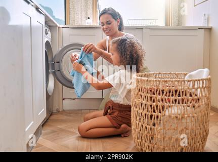 Junge hispanische Mutter und ihre Tochter sortieren schmutzige Wäsche in der Waschmaschine zu Hause. Ein bezauberndes kleines Mädchen und ihre Mutter machen Hausarbeiten zusammen Stockfoto