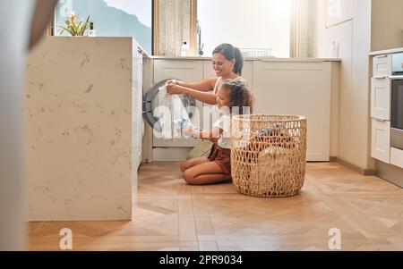 Junge hispanische Mutter und ihre Tochter sortieren schmutzige Wäsche in der Waschmaschine zu Hause. Ein bezauberndes kleines Mädchen und ihre Mutter machen Hausarbeiten zusammen Stockfoto