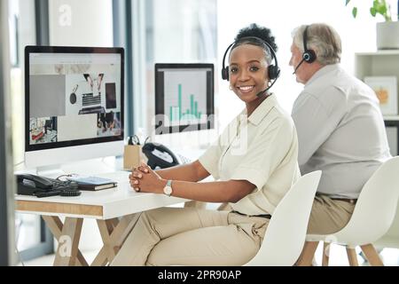 Ein Lächeln auf den Lippen bringt einen Anruf nach dem anderen. Eine attraktive junge Callcenter-Agentin sitzt mit ihrem Kollegen im Büro. Stockfoto