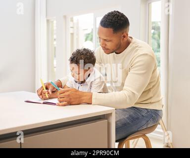 Vater gemischter Rasse, der seinem Sohn bei seinen Hausaufgaben hilft. Dad, der seinem Sohn Lesen und Schreiben beibringt, während der Schule. Kleiner Junge, der zu Hause sitzt, Eltern ist und zeichnet Stockfoto