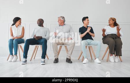 Sprechen über alle aktuellen heißen Themen. Eine Gruppe von verschiedenen Menschen, die miteinander reden, während sie vor weißem Hintergrund in einer Reihe sitzen. Stockfoto