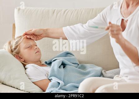 Heißer als die Sonne, auf eine schlechte Weise. Eine Mutter überprüft die Temperatur ihrer Töchter auf dem Sofa zu Hause. Stockfoto