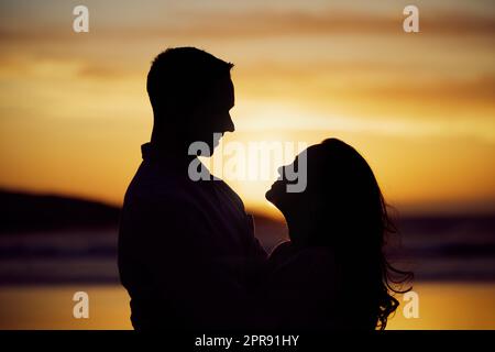 Silhouettenpaar, das romantische Momente genießt, von Angesicht zu Angesicht steht und bei Sonnenuntergang in die Augen blickt. Unbekannter Freund und Freundin, die sich verliebt haben, während sie sich am Strand anfreunden Stockfoto