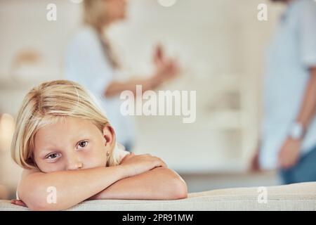 Porträt eines traurigen kleinen Mädchens, Eltern streiten im Hintergrund. Deprimiertes Kind, Eltern streiten zu Hause. Ein Paar, das sich um seine Tochter streitet. Gestresste, weiße Eltern, die sich scheiden lassen Stockfoto