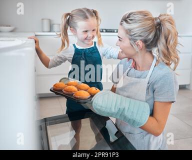 Mutter und Tochter nehmen Muffins aus dem Ofen. Glückliche Frau, die Muffins mit ihrer Tochter backt. Ein kleines Mädchen, das sich mit ihrer Mutter anfreundet und backt. Eltern nehmen Muffins aus dem Ofen Stockfoto