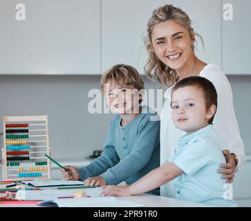 Porträt einer jungen, glücklichen, weißen Mutter, die ihren Söhnen zu Hause bei den Hausaufgaben hilft. Sorglose Geschwister, die lächeln, Spaß haben und mit ihrer mutter malen. Brüder machen Schularbeiten mit Hilfe von mom Stockfoto