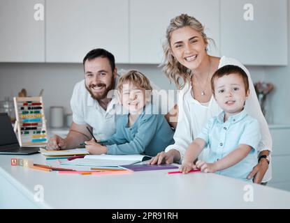 Junge, glückliche, weiße Familie, die zu Hause Spaß hat. Liebevolle Eltern helfen ihren kleinen Kindern bei Hausaufgaben. Sorglose Geschwister, die lächeln, während sie mit ihren eltern zeichnen Stockfoto