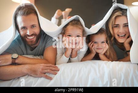 Porträt einer glücklichen weißen Familie, die zu Hause im Bett unter einer Decke lag. Fröhliche Geschwister entspannen sich im Bett mit ihren eltern im Schlafzimmer Stockfoto