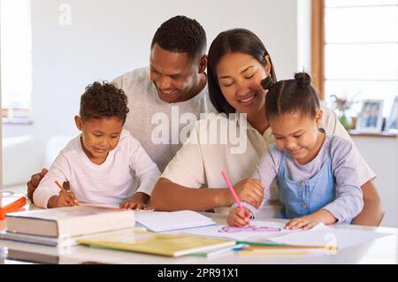 Glückliche kleine Kinder, die lernen und Hausaufgaben mit ihren Eltern machen. Gemischtes Rassen-Paar, das zu Hause einen Vorschulsohn und eine Tochter unterrichtete. Hispanische Mutter und Vater, die Kindern Schreibunterricht erteilen Stockfoto