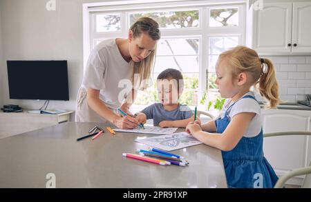 Junge, alleinstehende, weiße Mutter, die ihren zwei süßen kleinen Kindern bei ihren Hausaufgaben in einer hellen Küche hilft. Zwei Geschwister machen ihr Schulprojekt mit ihrer mutter zu Hause Stockfoto