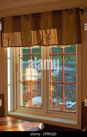 Alte Fensterwand im Vintage-Stil in einem Wohngebäude. Hintergrund des Außengeländes mit Licht, das in die Fenster scheint. Holzrahmenkonstruktion mit schützenden Stahlstangen und alten Schlössern an Holzrahmen. Stockfoto