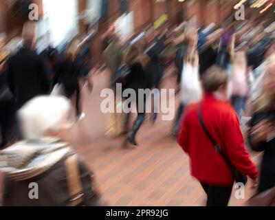 Eine Gruppe von Personen, die mit unscharfen Bewegungen durch städtische Straßen pendeln. Eine geschäftige Menschenmenge von Reisenden, die in einer Straße in der Stadt ankommen und zusammen spazieren. Viele Touristen in der Innenstadt Stockfoto