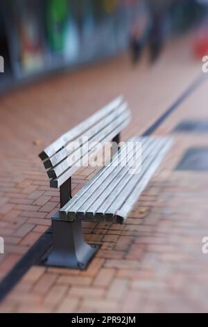 Landschaft mit leerer Straßenbank aus Holz. Abgelegene und verwitterte öffentliche Holzbank im Freien mit verschwommenem Hintergrund und Kopierbereich auf einem Gehweg. Sitzgelegenheiten im Vintage-Stil, perfekt zum Ausruhen. Stockfoto