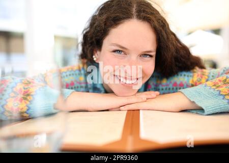 Eine glückliche Frau, die dich über eine Speisekarte in einer Bar ansieht Stockfoto