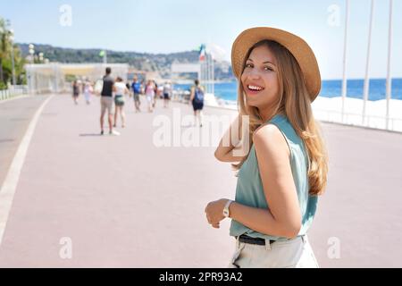 Porträt einer attraktiven Modefrau dreht sich um und lächelt der Kamera zu, die entlang der Promenade des Anglais, Nizza, Frankreich, läuft Stockfoto