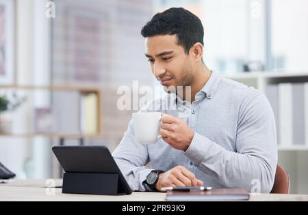 So starte ich meinen Tag. Ein junger Geschäftsmann trinkt Kaffee, während er sein digitales Tablet benutzt. Stockfoto