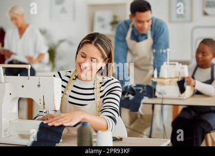 Glückliche und lächelnde weibliche Schneiderin, die in der Textilfabrik an Design und Nähgewebe arbeitet. Eine freudige Designerin und Schneiderin bei der Reparatur von Kleidung in einer Werkstatt. Stockfoto