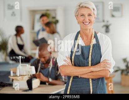 Selbstbewusste leitende Lehrerin für Kleiderproduktion, die über ihren Erfolg lächelt. Stolzer moderner Modeunternehmer, der ein Unternehmen gründet. Porträt einer alten Frau, die Erwachsenen eine Schneiderberufsausbildung gibt Stockfoto