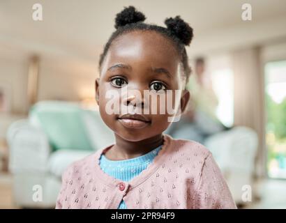 Unübertroffene Niedlichkeit. Ein Porträt eines entzückenden kleinen Mädchens mit Zöpfen, die zu Hause auf dem Boden des Wohnzimmers sitzen. Stockfoto