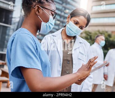 Es ist so einfach wie ein Fingertipp. Zwei junge Ärztinnen mit einem digitalen Tablet in der Stadt. Stockfoto