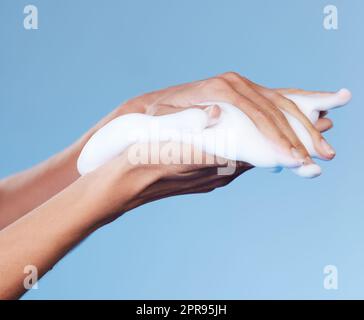 Aufschäumen für weiche, glatte Haut. Studio-Aufnahme einer unkenntlichen Frau, die vor blauem Hintergrund Seife auf ihren Händen rieb. Stockfoto