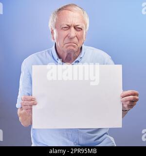 Also nicht cool. Studioaufnahme eines älteren Mannes, der ein leeres Schild in der Hand hält und vor blauem Hintergrund unglücklich aussieht. Stockfoto