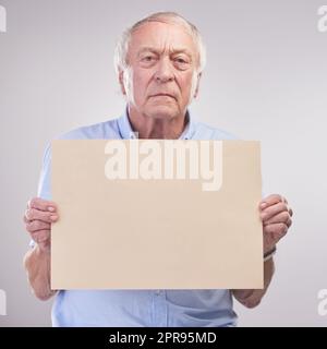 Hört zu, Leute... Studioaufnahme eines älteren Mannes mit einem leeren Schild vor grauem Hintergrund. Stockfoto