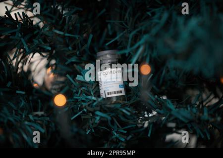 Geben Sie Ihren Lieben das Geschenk der Impfung. Eine Impfstoffflasche auf einem Baum während der Weihnachtszeit. Stockfoto