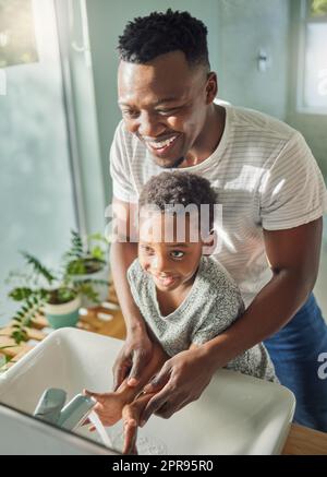 Eine saubere Nation beginnt zu Hause. Ein Vater hilft seinem Sohn, sich die Hände am Wasserhahn in einem Badezimmer zu Hause zu waschen. Stockfoto