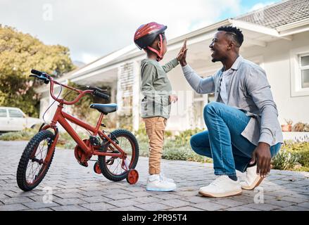 Ein Vater und sein Sohn geben sich gegenseitig eine hohe fünf, während sie mit dem Fahrrad im Freien fahren. Stockfoto