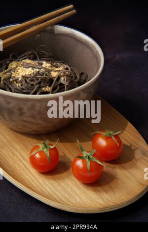 Exquisites Gericht mit schwarzen Nudeln mit einem Hauch von Eleganz. Die Nahaufnahme einer leuchtend roten Kirschtomate ist perfekt auf den Hintergrund der Delikatessen abgestimmt Stockfoto