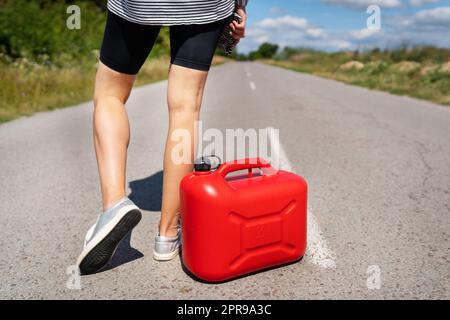 Ein Auto, das am Straßenrand geparkt ist, ein leerer roter Kanister. Das Mädchen hält auf der Straße an, um das Auto zu betanken. Kraftstoffmangel - Öl, Diesel, Benzin. Stockfoto