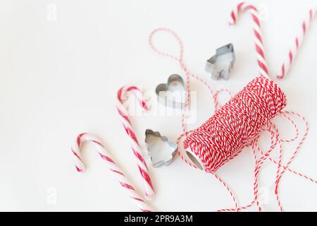 Weihnachtsbonbons, Keksschneider, roter Faden für Geschenkverpackungen, liegen auf einem weißen Tisch. Weihnachten und Silvester 2023-2024. Stockfoto